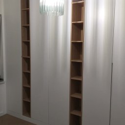 MARTINOS MEBLE NA WYMIAR Marcin Hełmiński - Biała szafa wnękowa z drewnianymi półkami, oświetlona lampą z dekoracyjnym kloszem, na parkiecie ułożonym w jodełkę. Minimalistyczny design.