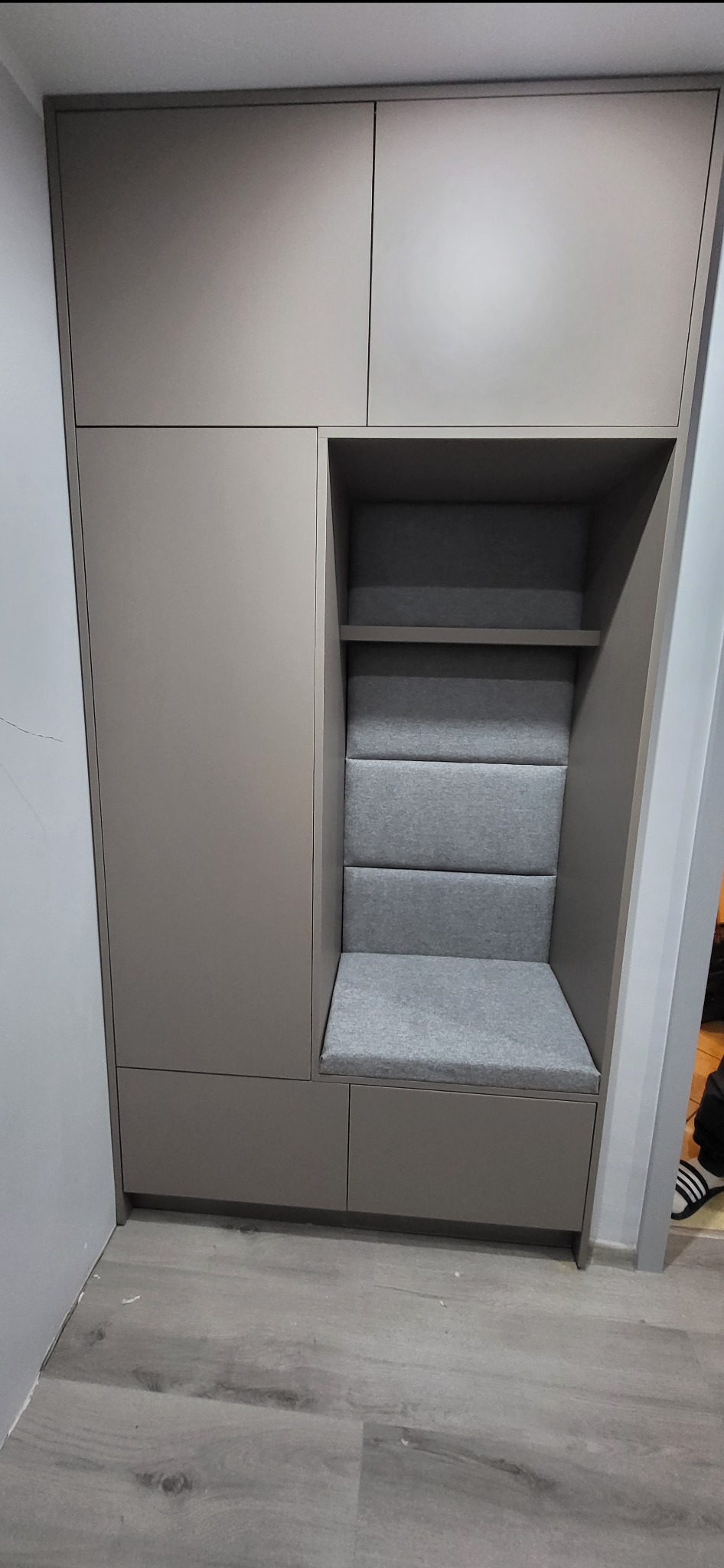 Beżowa szafa wnękowa z siedziskiem obitym szarą tkaniną. Siedzisko z półką. Nowoczesny design, minimalistyczny styl.