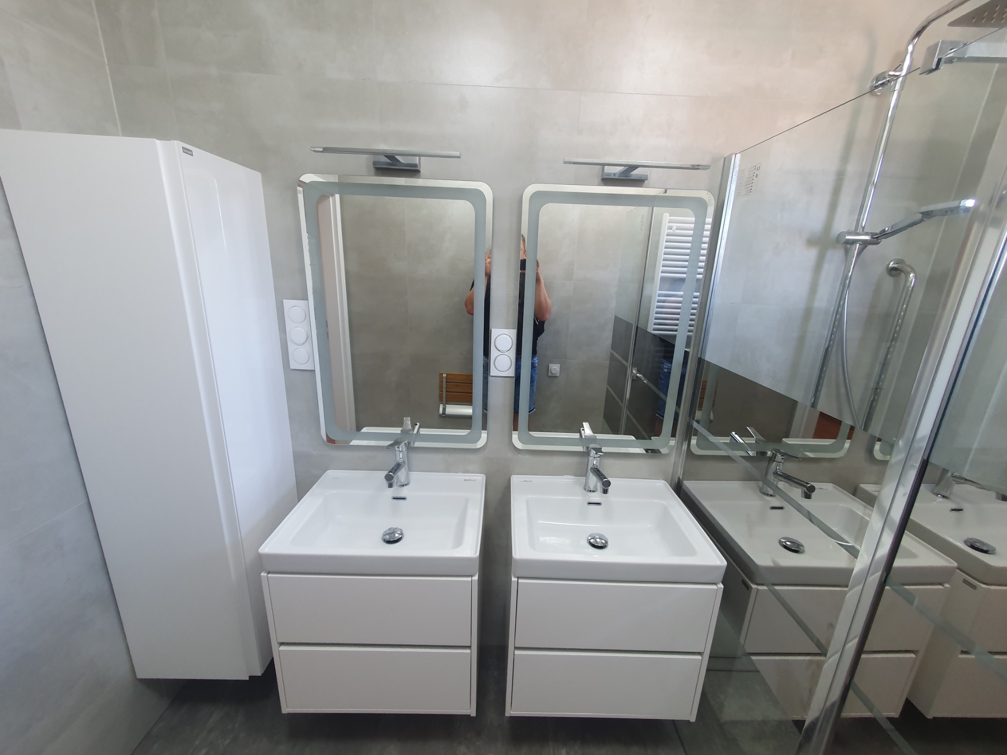 Jasna łazienka z dwiema umywalkami nablatowymi, szafkami pod umywalki z szufladami, lustrami z podświetleniem LED oraz kabiną prysznicową ze szklaną ścianką.