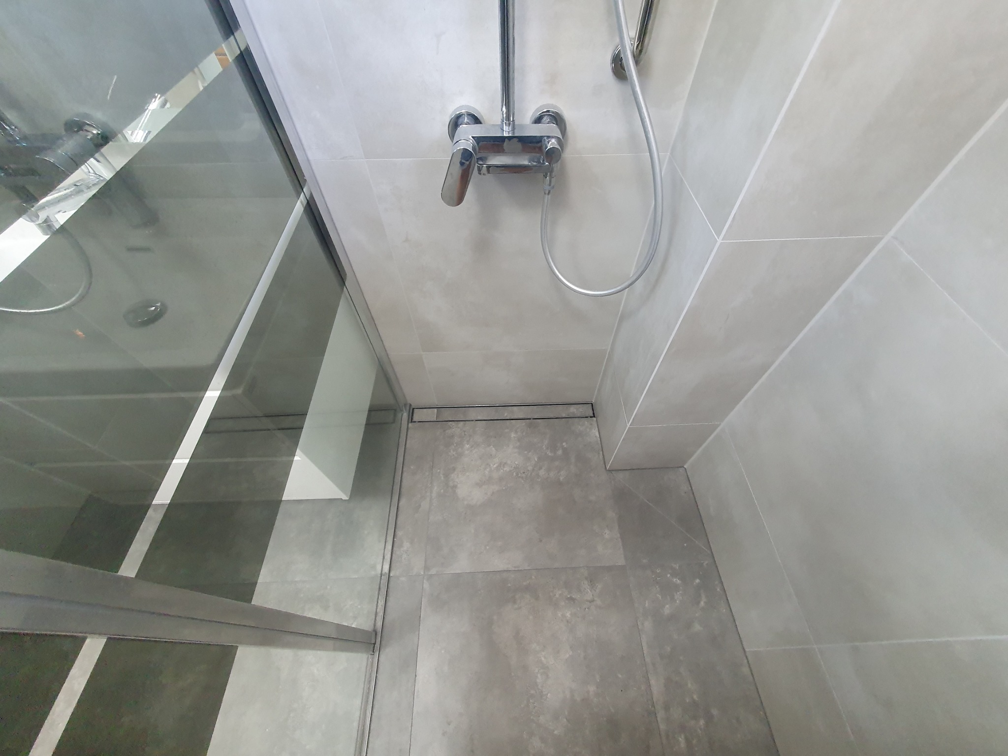 Nowoczesna kabina prysznicowa z szarymi płytkami, chromowaną armaturą i odpływem liniowym w podłodze.