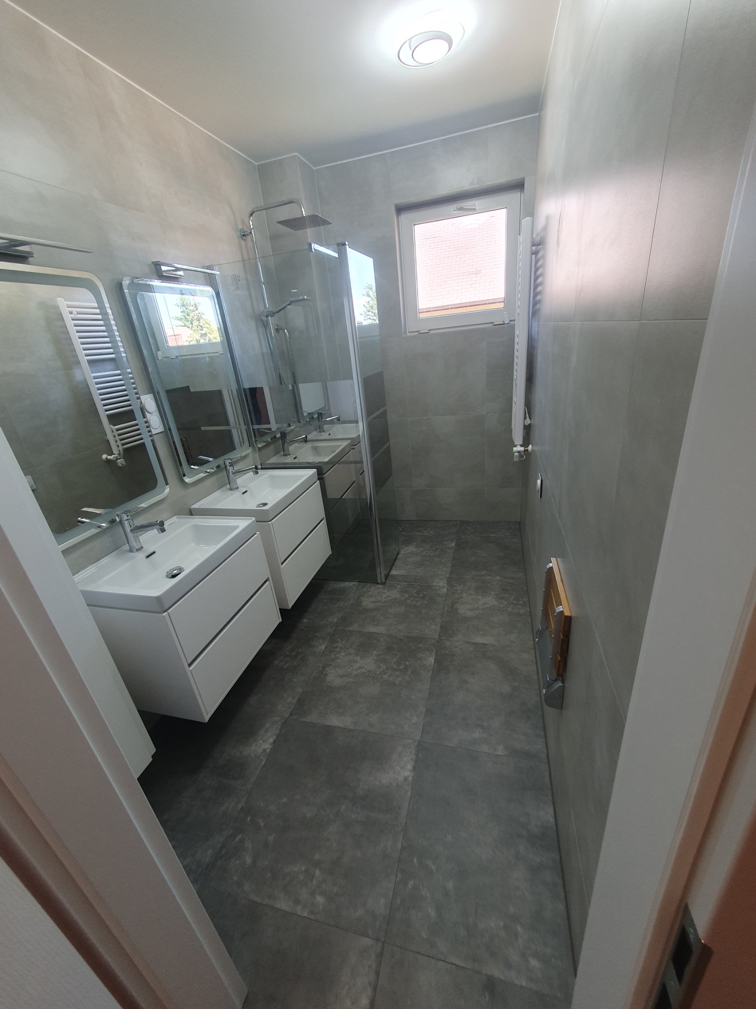 Nowoczesna łazienka w szarościach z dwoma umywalkami na białych szafkach, kabiną prysznicową typu walk-in i grzejnikiem drabinkowym.