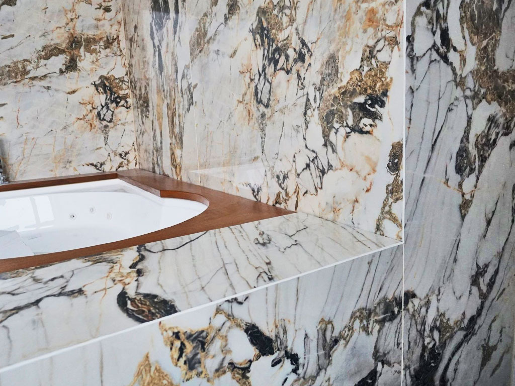 Wykończona łazienka z wanną jacuzzi obłożoną marmurem o unikalnym wzorze z brązowymi i czarnymi żyłami, drewniane obramowanie wanny.