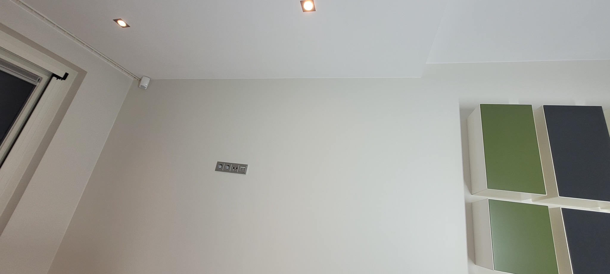 Jasne wnętrze po odświeżeniu ścian, widoczne gładkie powierzchnie, nowoczesne oświetlenie sufitowe, gniazdka elektryczne oraz dekoracyjne panele ścienne w kolorach zieleni i grafitu.