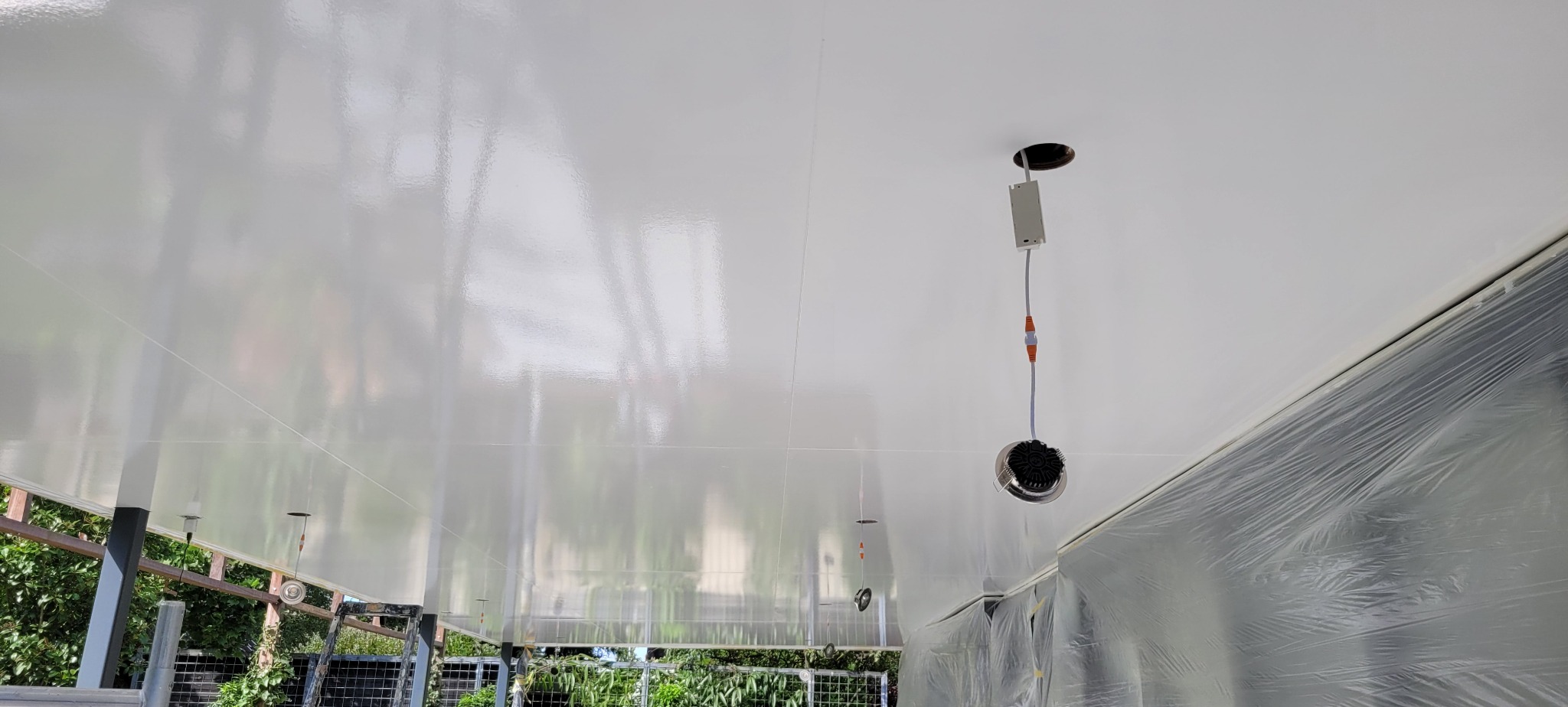 Błyszczący, świeżo pomalowany sufit w trakcie instalacji oświetlenia punktowego, ściany częściowo zabezpieczone folią ochronną.