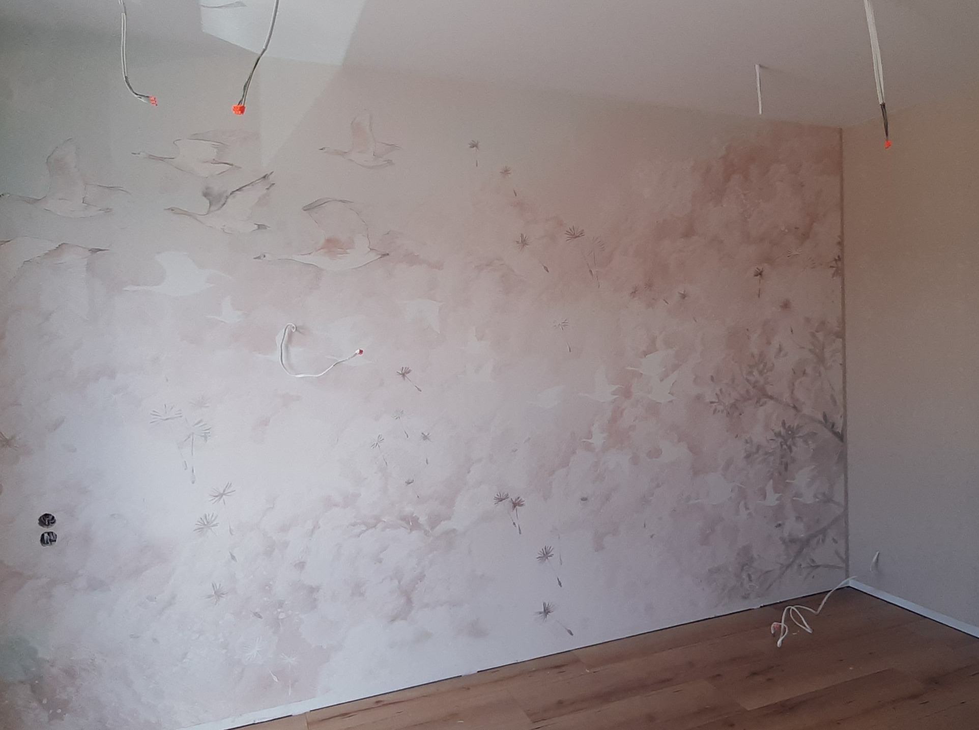 Pokój po malowaniu z motywem ptaków i roślin na ścianie, widoczne wystające kable. Jasne panele podłogowe.