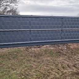 Usługi Spawalnicze - Przesuwna brama wjazdowa z poziomymi panelami kompozytowymi w kolorze grafitowym, zamontowana między betonowymi słupkami, na tle błotnistego trawnika i pochmurnego nieba.