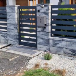 Usługi Spawalnicze - Nowoczesne ogrodzenie panelowe z poziomymi przęsłami w kolorze grafitowym, osadzone na murku z szarych bloczków imitujących kamień, z małym ogródkiem z białym grysem i nasadzeniami lawendy.