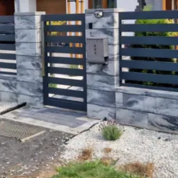 Nowoczesne ogrodzenie panelowe z poziomymi przęsłami w kolorze grafitowym, osadzone na murku z szarych bloczków imitujących kamień, z małym ogródkiem z białym grysem i nasadzeniami lawendy.