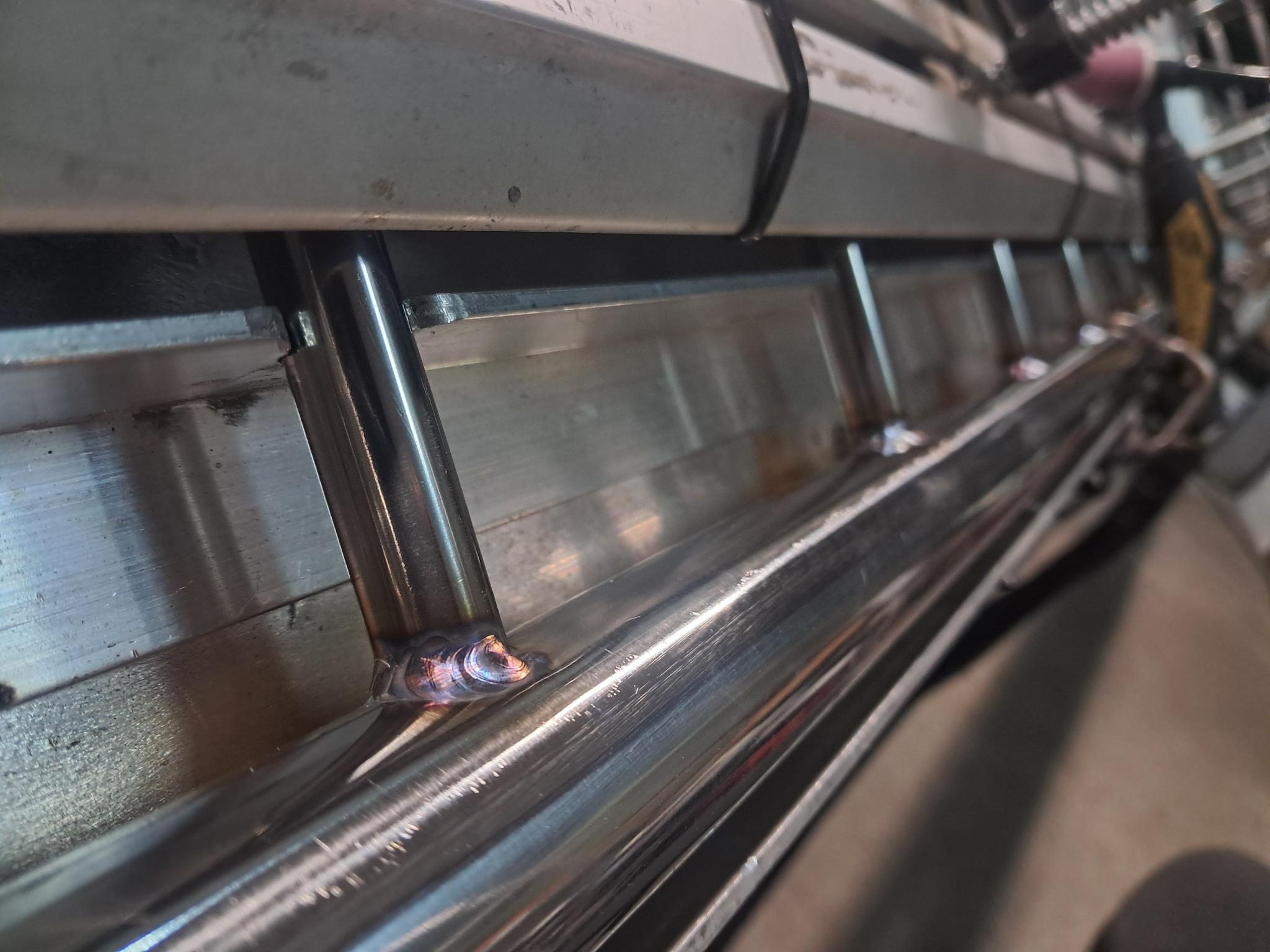 Detal spawu ramy metalowej konstrukcji z okrągłych profili, widoczne ślady spawania i obróbki metalu.