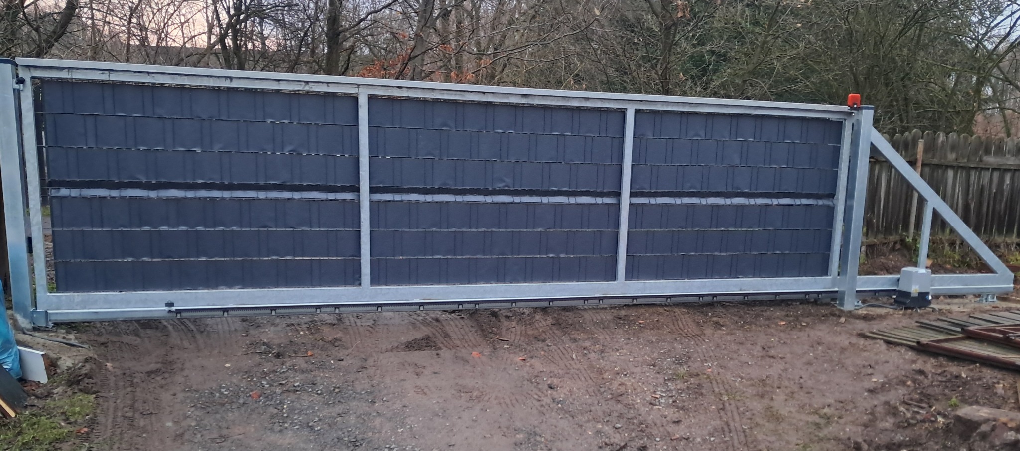 Przesuwna brama wjazdowa z szarym wypełnieniem panelowym i automatyką, widoczny silnik i lampa ostrzegawcza, teren po montażu.