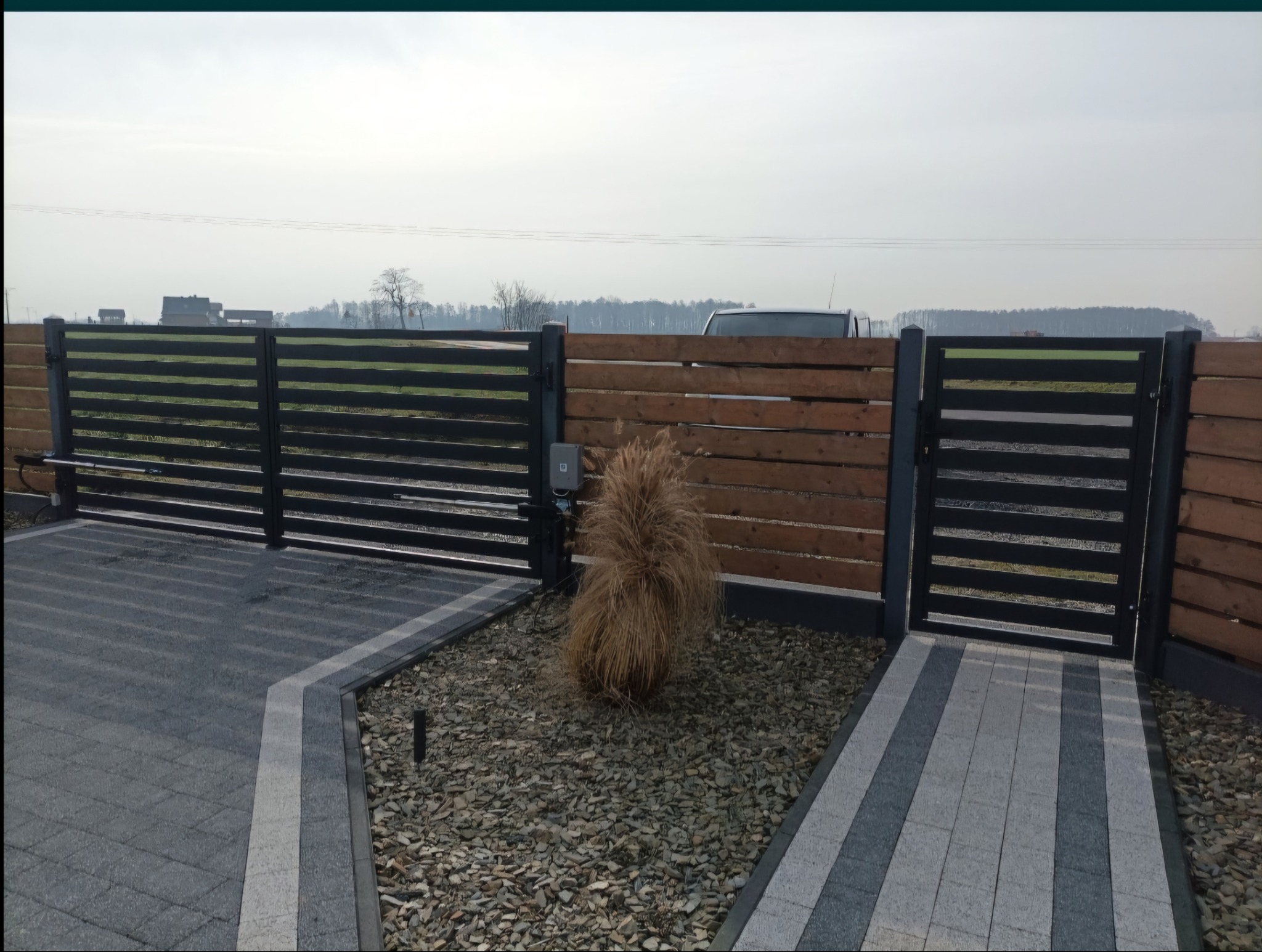 Nowoczesna brama wjazdowa i furtka z poziomych profili, uzupełnione drewnianym ogrodzeniem, z automatyką, na podjeździe z kostki brukowej