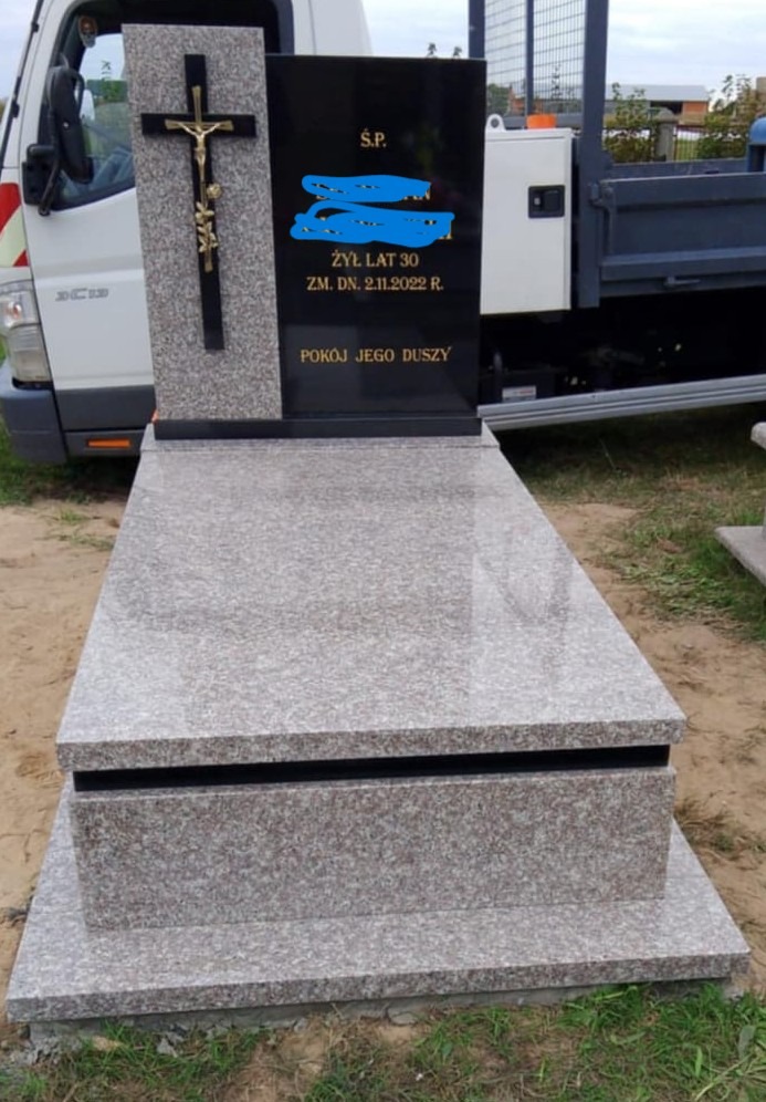 Granitowy nagrobek z krzyżem i czarną tablicą inskrypcyjną, na tle białego samochodu dostawczego, prezentuje kamieniarską precyzję i dbałość o detale.