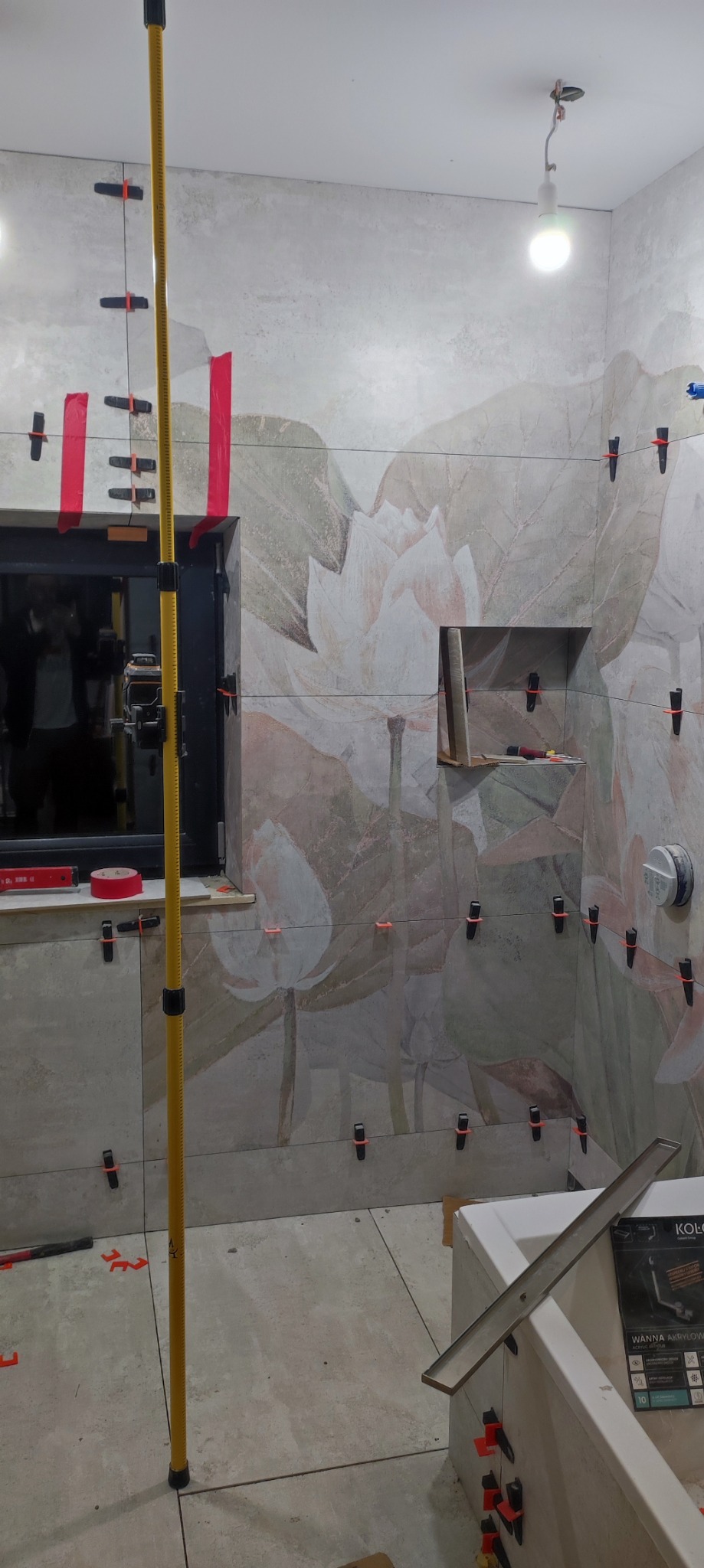 Łazienka w trakcie układania płytek z motywem kwiatowym, widoczne poziomice, listwy i system poziomowania płytek.