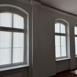 GREEN HOUSE Plejada-Stary Nowy Dom - Trzy okna z białymi, plisowanymi osłonami okiennymi w klasycznym wnętrzu z listwami przysufitowymi.