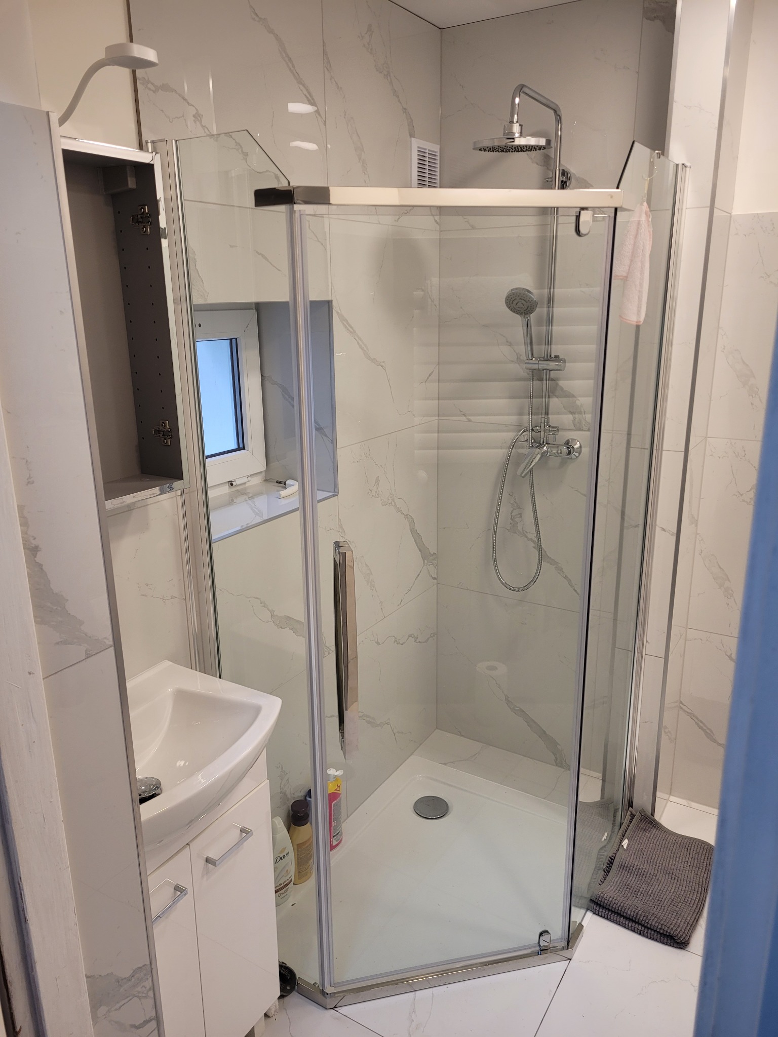 Nowoczesna łazienka z kabiną prysznicową narożną, umywalką na szafce i marmurowymi płytkami ściennymi.