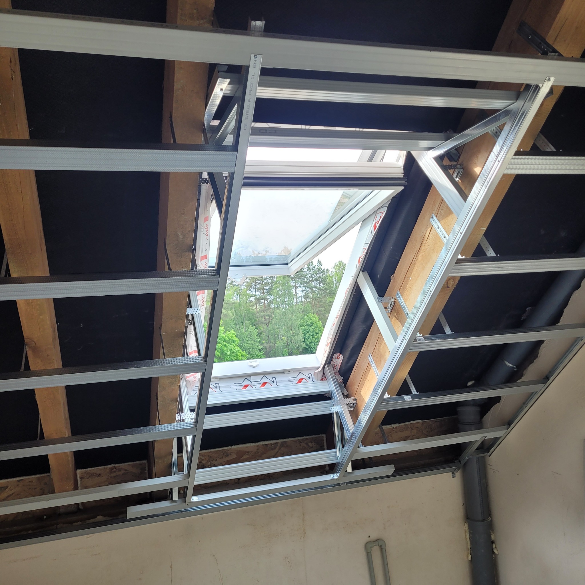 Montaż okna dachowego w trakcie tworzenia konstrukcji z profili metalowych, widok na zewnątrz przez otwarte okno