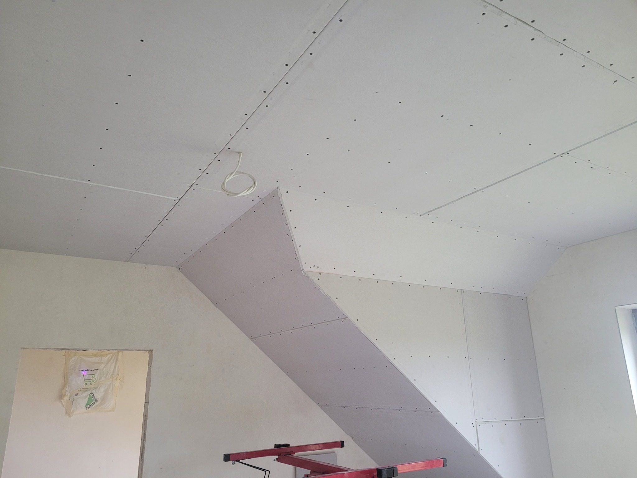 Montaż płyt kartonowo-gipsowych na poddaszu, widoczne łączenia płyt i kabel oświetleniowy wystający z sufitu.