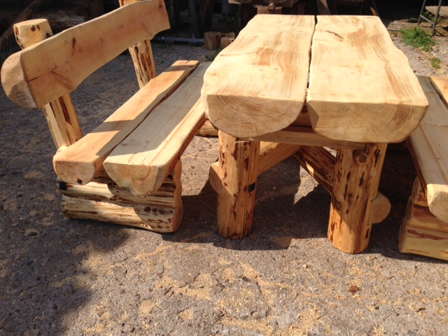 Rustykalny zestaw mebli ogrodowych z surowego drewna: ławka z oparciem i stół z blatem z dwóch desek, widoczne słoje i naturalna kora.