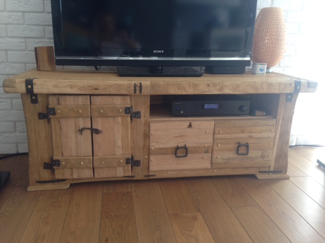 Rustykalna szafka RTV z litego drewna z metalowymi okuciami, na podłodze z paneli, pod telewizorem Sony. Widoczny sprzęt audio.