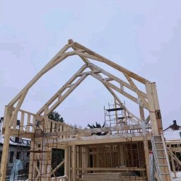 RakMik sp.z.o.o - Konstrukcja drewniana domu w trakcie budowy, widoczne rusztowania i drabina, zimowa sceneria z pokrywą śnieżną.