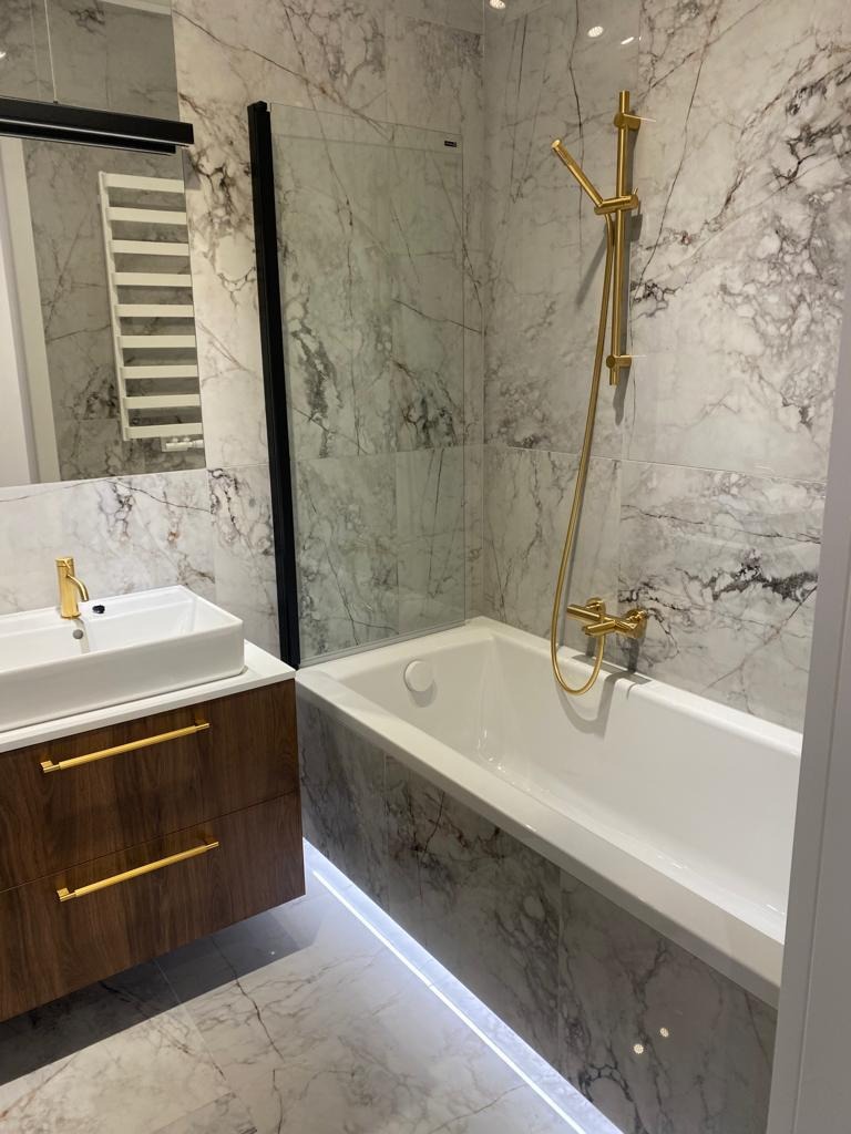 Nowoczesna łazienka z marmurowymi płytkami, złotą armaturą i podświetlaną wanną LED.