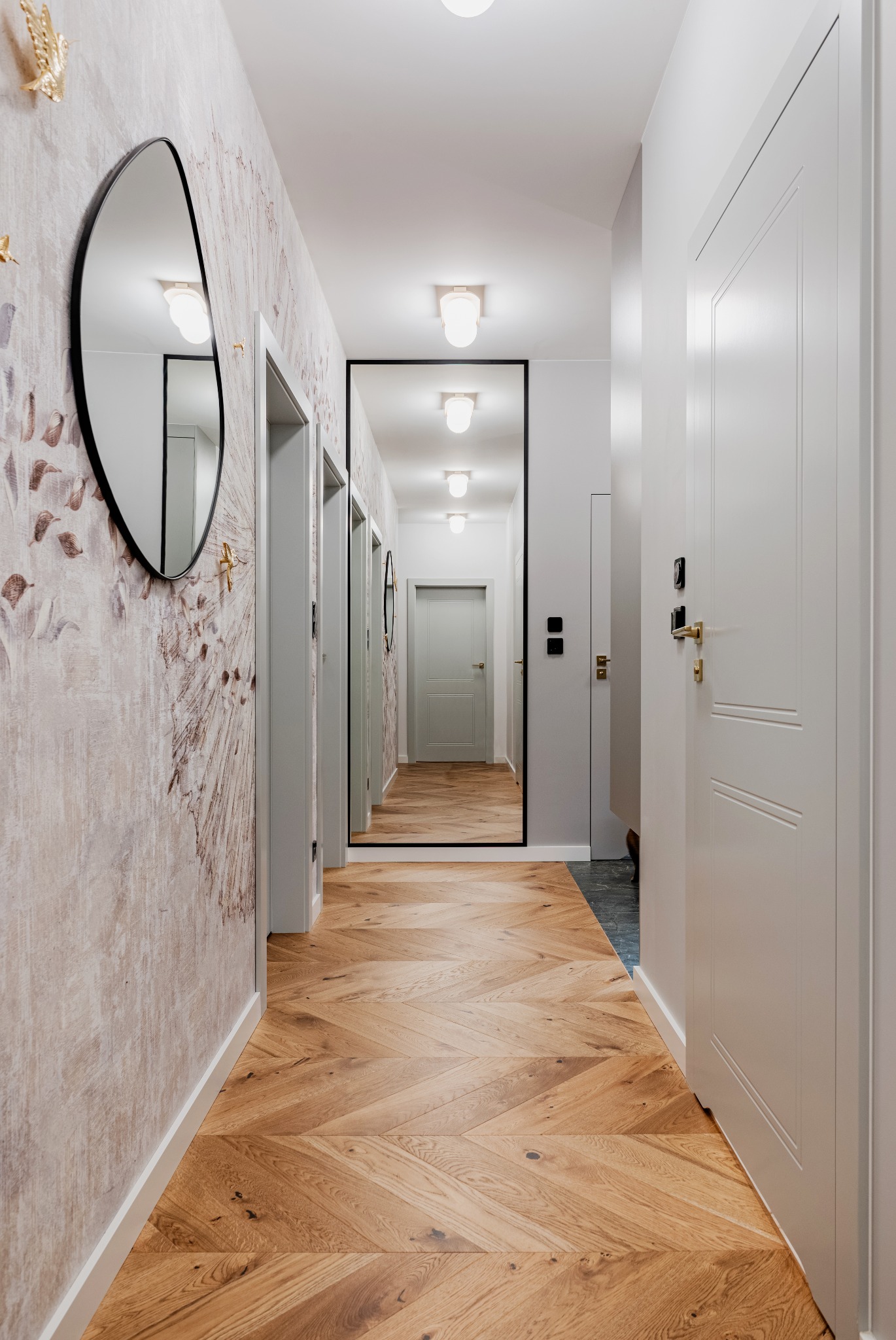 Wąski korytarz z parkietem w jodełkę, lustrem w czarnej ramie na końcu, tapetą w stylu akwareli i złotymi wieszakami w kształcie ptaków.