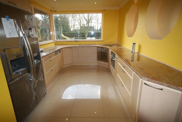 Jasna kuchnia z blatem kamiennym w odcieniach brązu, widok na okno z ogrodem. Nowoczesny design z żółtymi ścianami i dużym, srebrnym холодильником.