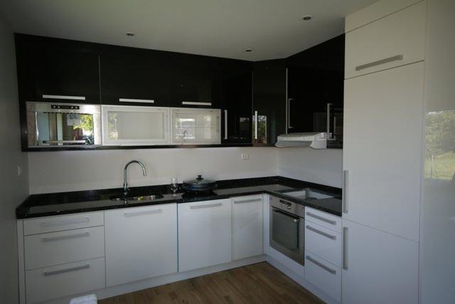 Nowoczesna kuchnia w bieli i czerni z blatem z czarnego kamienia. Uwagę przykuwają błyszczące fronty szafek i drewniana podłoga. Widoczny zlew, bateria i płyta grzewcza.