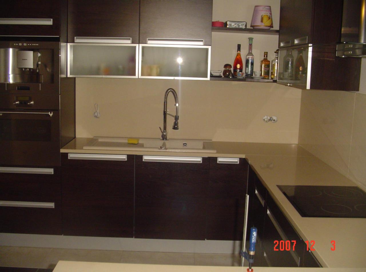 Kuchnia z ciemnymi szafkami i blatem z konglomeratu, widoczny zlew i płyta indukcyjna. Ujęcie wnętrza, oświetlenie punktowe.