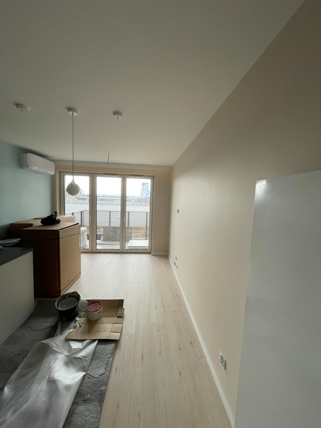 Wnętrze mieszkania w trakcie prac wykończeniowych: świeżo pomalowane ściany w odcieniach beżu i błękitu, położone panele podłogowe, zabezpieczona folią podłoga, widoczne puszki z farbą i kartony...