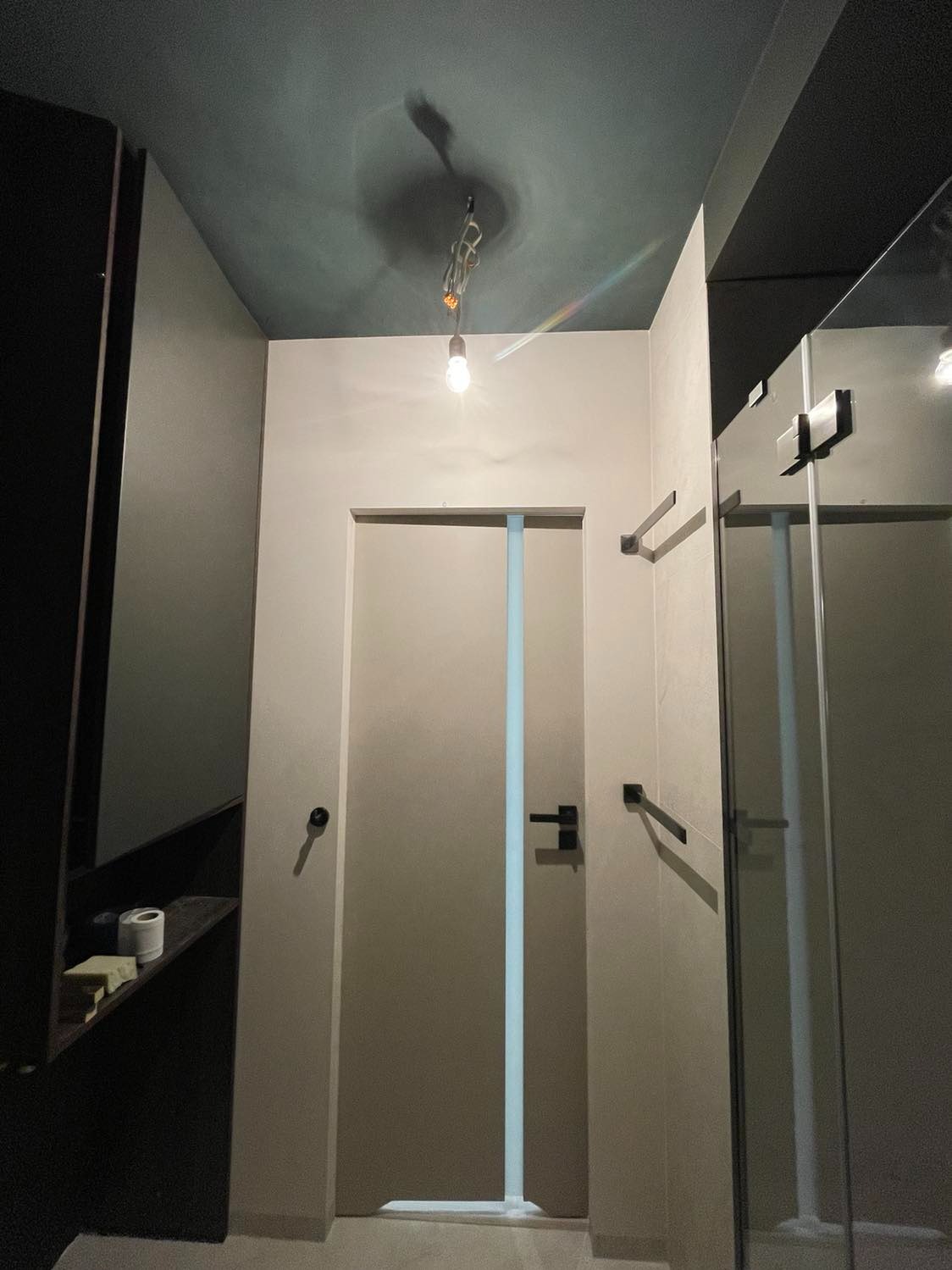 Nowoczesna łazienka z kabiną prysznicową i oświetleniem punktowym, widoczne detale wykończenia ścian i sufitu w odcieniach szarości i zieleni, minimalistyczne akcesoria łazienkowe.