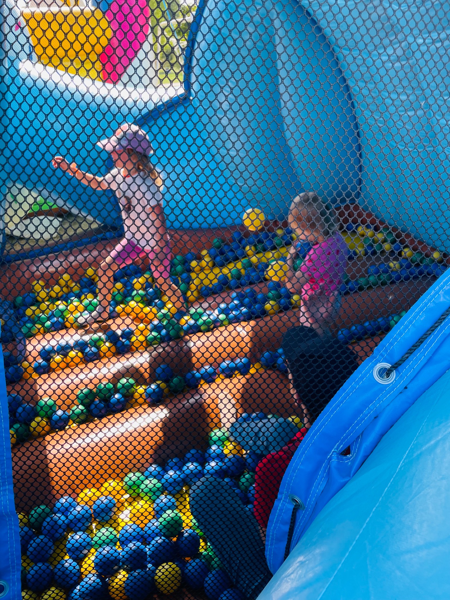 Dzieci bawią się w dmuchanym zamku z basenem wypełnionym kolorowymi piłeczkami. Widok przez siatkę ochronną, ujęcie z dołu.