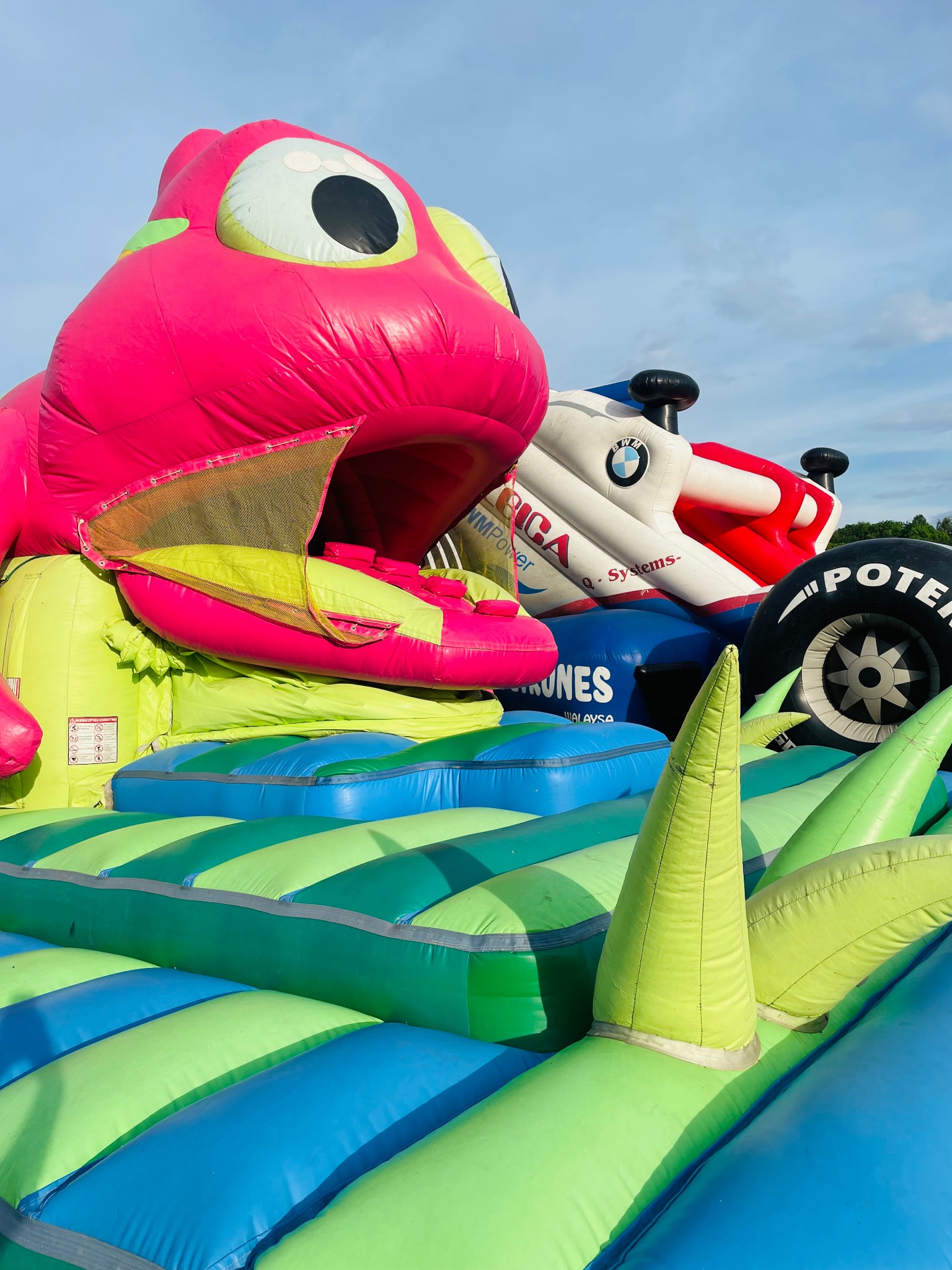 Kolorowy dmuchany plac zabaw z motywem zwierząt i aut, idealny na imprezy plenerowe. Widoczne elementy w odcieniach różu, zieleni i niebieskiego.