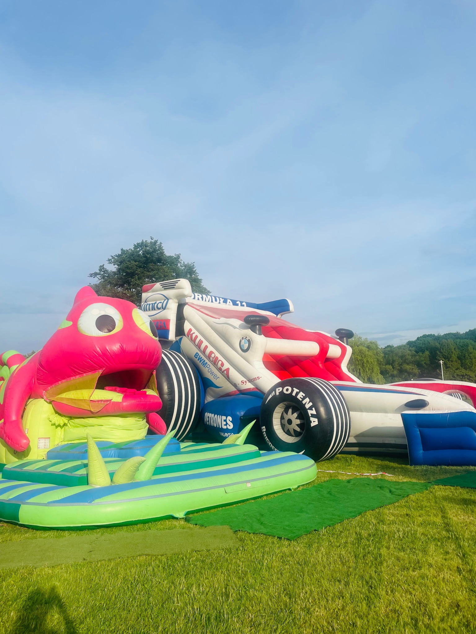 Kolorowy dmuchany tor przeszkód w kształcie bolidu Formuły 1 i żaby na trawie, atrakcja eventowa dla dzieci.