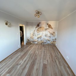 DIM BUD DMYTRO PUKSHYN - Pusty pokój po remoncie z nową podłogą z paneli w odcieniach brązu, ozdobną tapetą z motywem roślinnym na jednej ścianie i nowoczesnym oświetleniem.