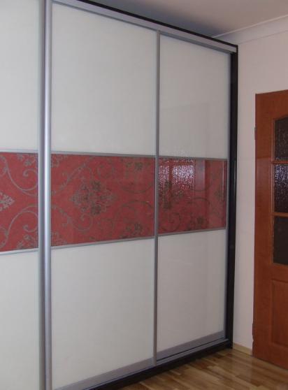 Trzydrzwiowa szafa przesuwna z białymi panelami i poziomym pasem czerwonej tapety w kwiaty, srebrne obramowanie, widoczna część drewnianej podłogi i drzwi.