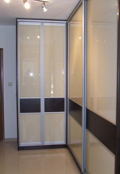 Wnętrze z dwiema szafami z przesuwnymi drzwiami, beżowo-brązowe panele na frontach, oświetlenie punktowe na suficie.