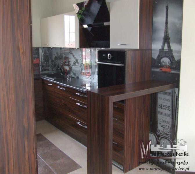 Nowoczesna kuchnia z frontami z ciemnego drewna, białymi szafkami wiszącymi i szklanym panelem z motywem miejskim oraz grafiką wieży Eiffla.