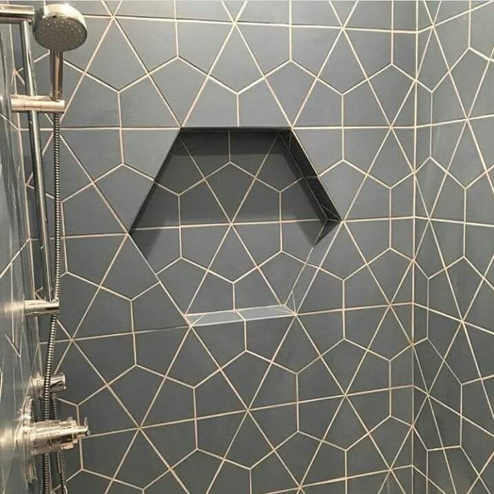 Niebiesko-szara ściana kabiny prysznicowej z geometrycznym wzorem płytek i wnęką w kształcie sześciokąta, widoczny zestaw prysznicowy ze stali nierdzewnej.