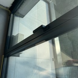 Korz-bud - Szczegółowe ujęcie ramy okiennej z widokiem na płytki balkonu i odbijające się niebo, ukazujące precyzję montażu i estetykę wykończenia.