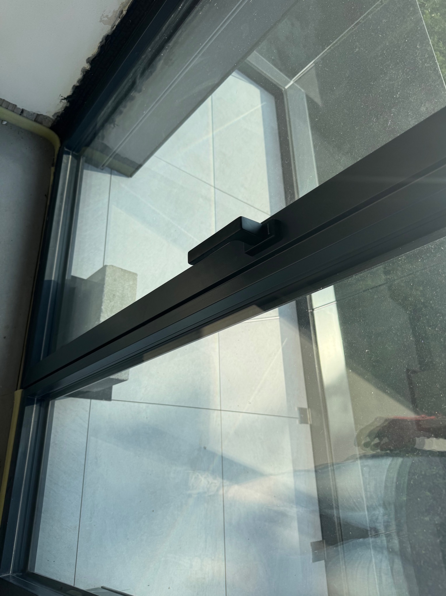 Szczegółowe ujęcie ramy okiennej z widokiem na płytki balkonu i odbijające się niebo, ukazujące precyzję montażu i estetykę wykończenia.