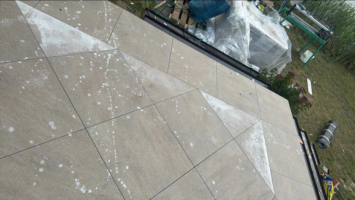 Ułożona, betonowa podłoga tarasu z geometrycznym wzorem, zabrudzona zaprawą. W tle narzędzia i materiały budowlane. Widok z góry na ukośnej płaszczyźnie.