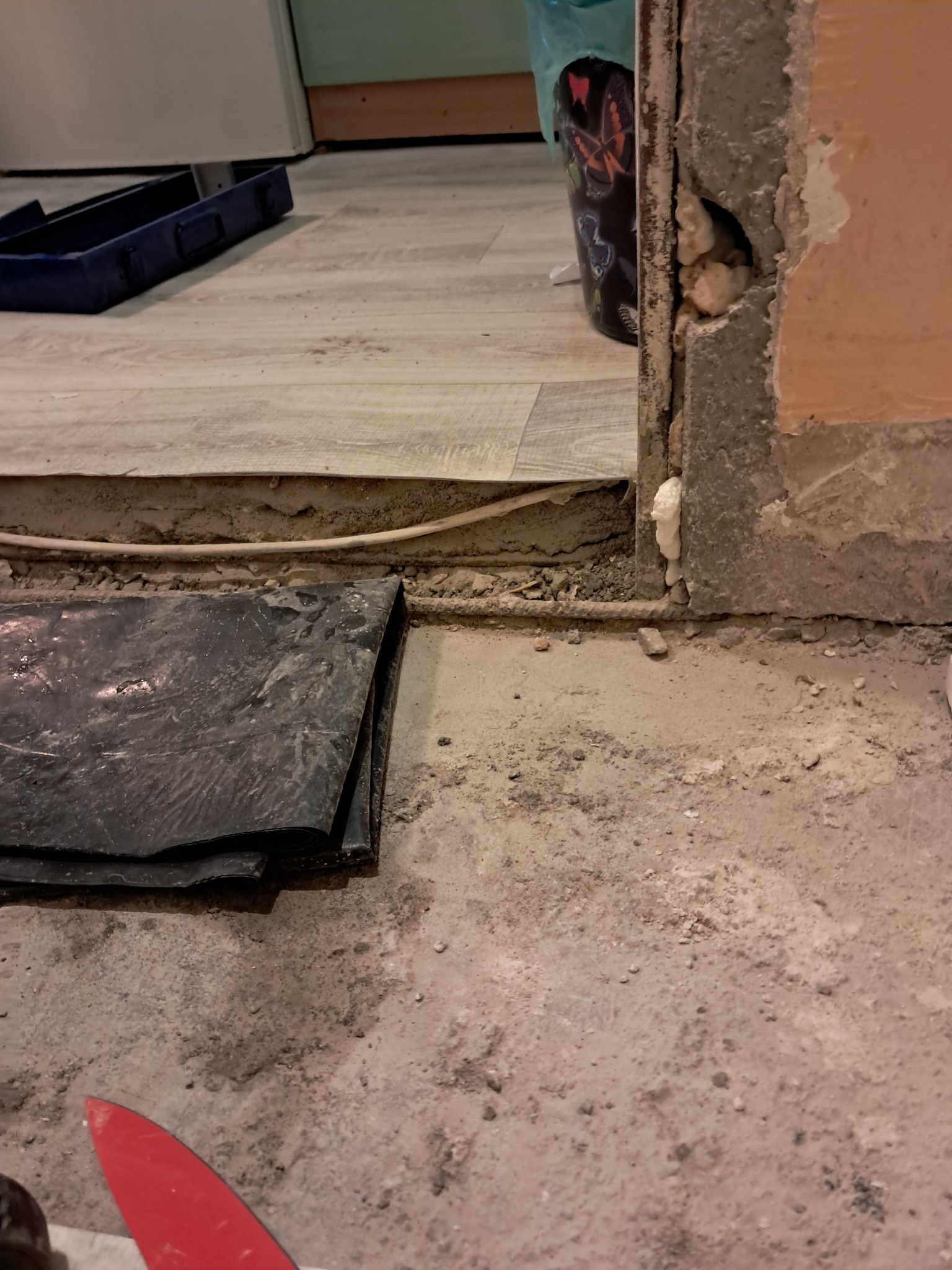 Przygotowanie do położenia paneli: widoczna podłoga z wylewką, fragment położonych paneli, folia izolacyjna, kabel oraz fragment ściany z pianką montażową.