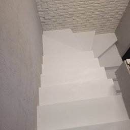 Mikrocement i hydroizolacje - Białe schody pomalowane farbą, widok z góry, ściana z efektem cegły w tle, jasne wnętrze.