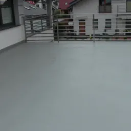 Szary, gładki taras z metalową balustradą, widok na sąsiednie domy z czerwonymi dachami.