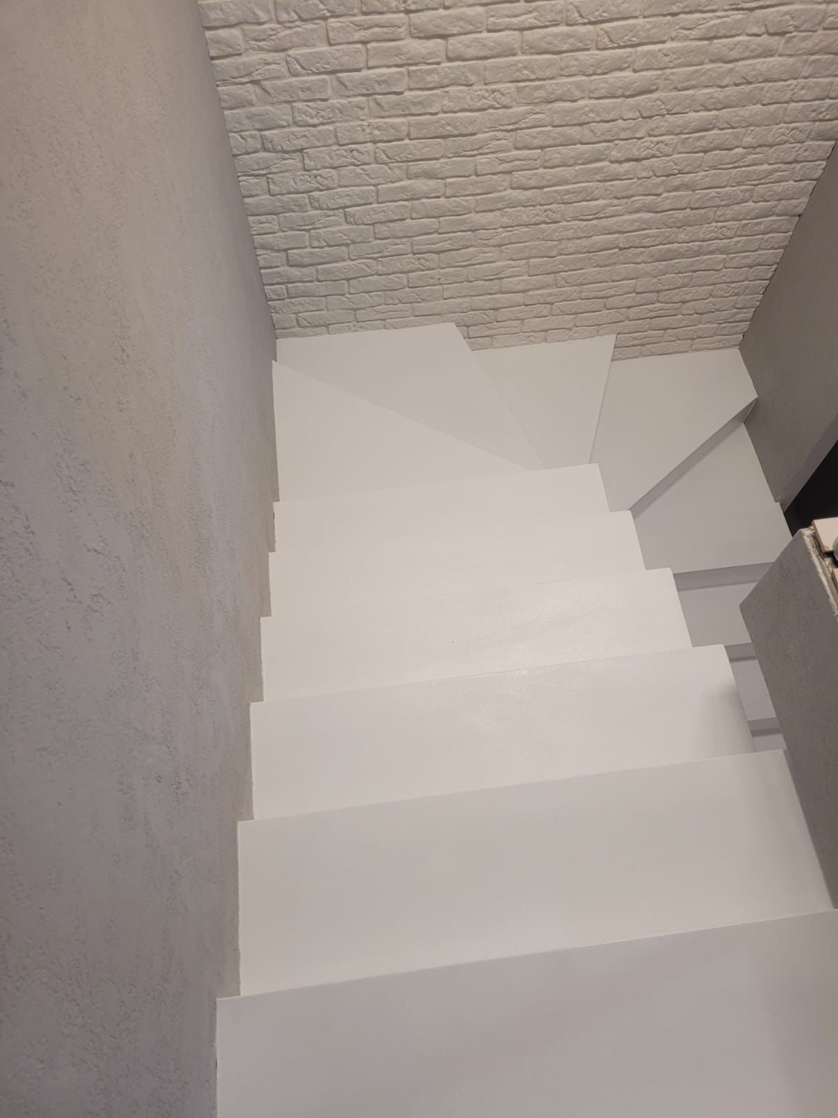 Białe schody pomalowane farbą, widok z góry, ściana z efektem cegły w tle, jasne wnętrze.