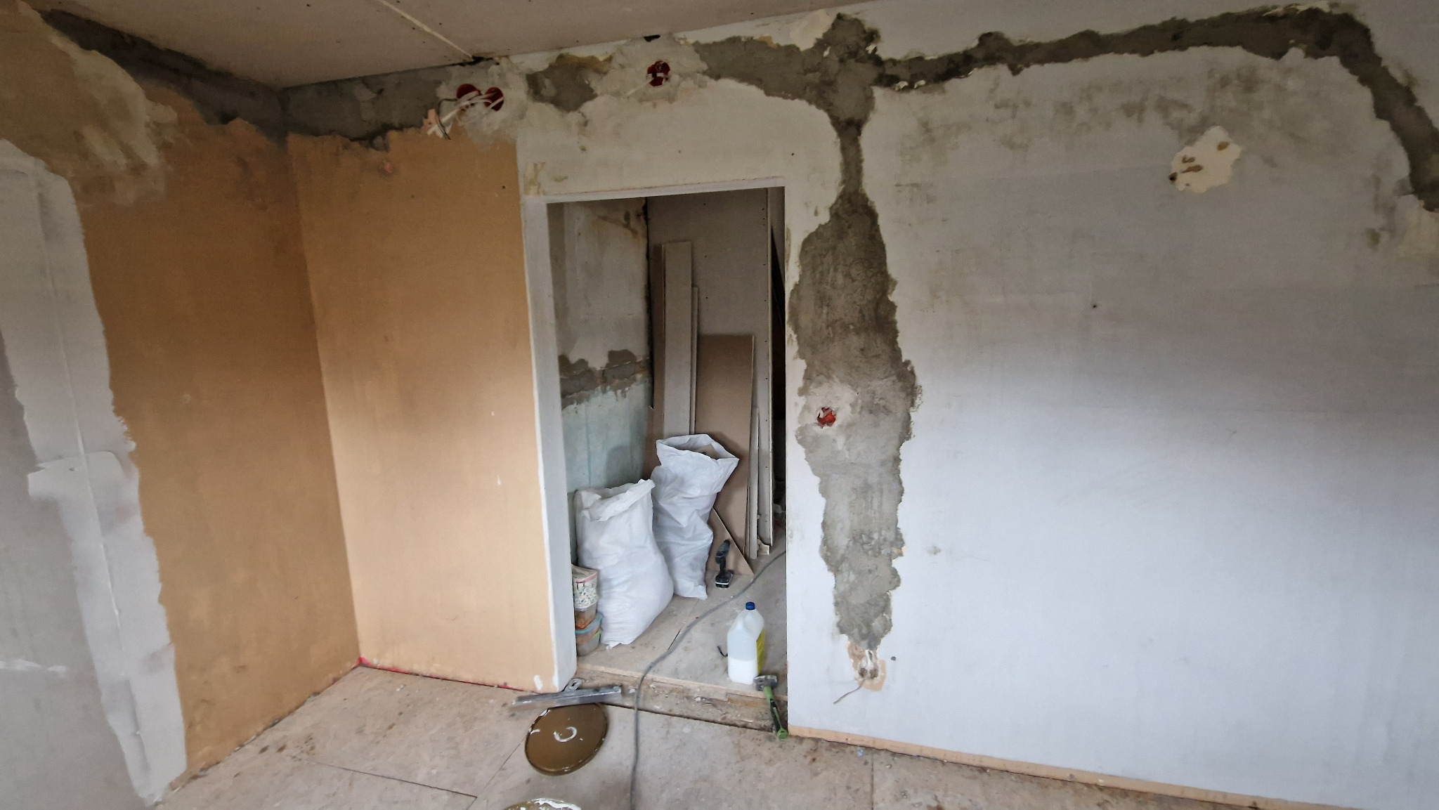 Wnętrze w Kłodzku w trakcie prac przygotowawczych do remontu: ściany z widocznymi śladami po kuciu, worki z materiałami budowlanymi w przejściu, widoczne przewody elektryczne.