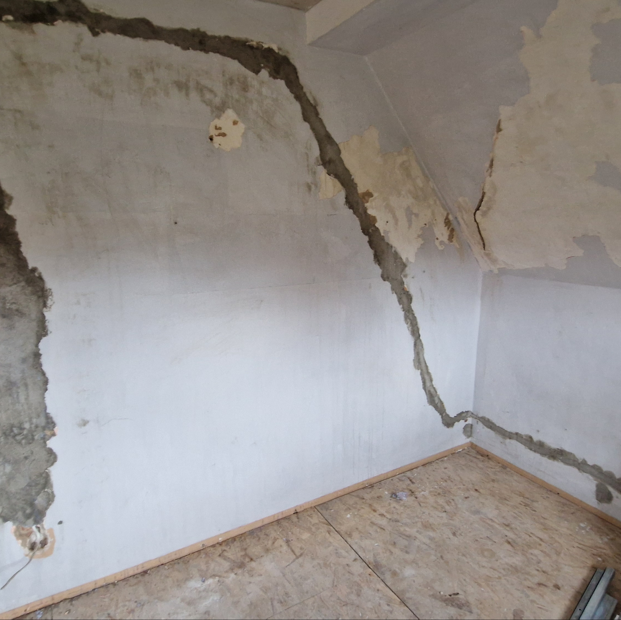 Pokój w trakcie remontu: ściany z resztkami starej farby i szpachli, widoczne ślady po instalacjach elektrycznych, surowa podłoga z płyt OSB.