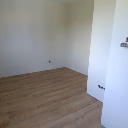 Remontowo Sebastian Sandomierski - Jasne panele podłogowe ułożone w pustym, świeżo pomalowanym pokoju z widocznymi gniazdkami elektrycznymi. Minimalistyczne wykończenie wnętrza.