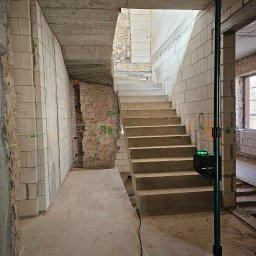 Market Group Sp. z o. o. - Wnętrze w trakcie remontu: surowe ściany z betonu komórkowego i cegły, betonowe schody, zielony laser krzyżowy wyznaczający poziom. Widoczne ślady po instalacjach.